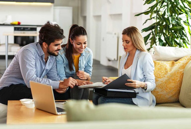 A person reviews a credit score report at a kitchen table beside insurance documents and a laptop.